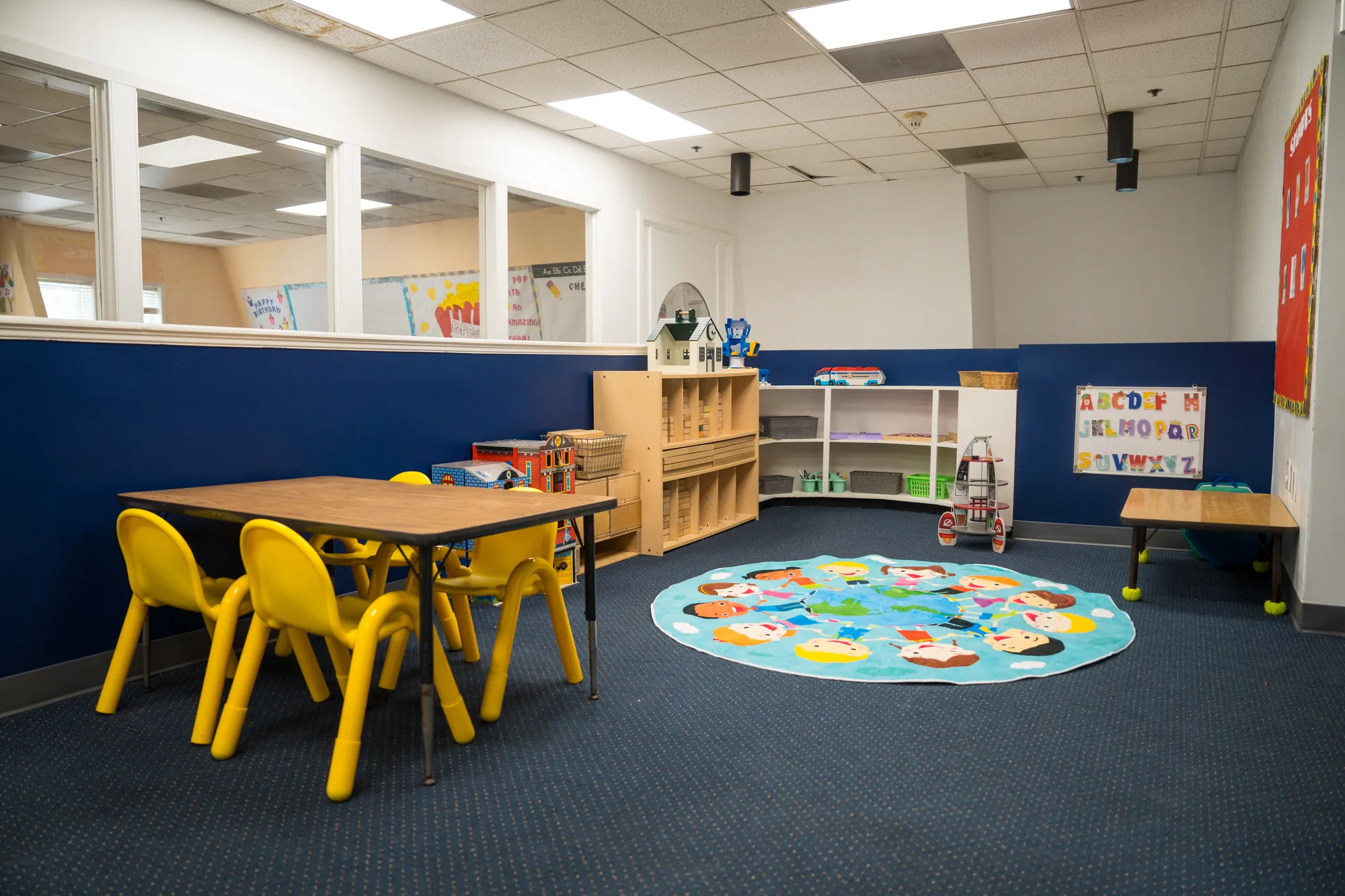 Shared activity area with yellow chairs, low shelving, and a world map rug