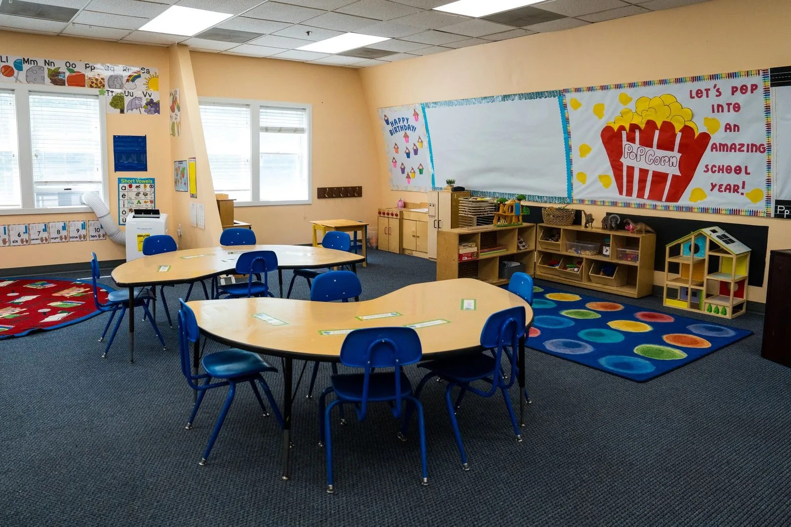 Pre-K work tables with blue chairs, the circles rug, and the doll house